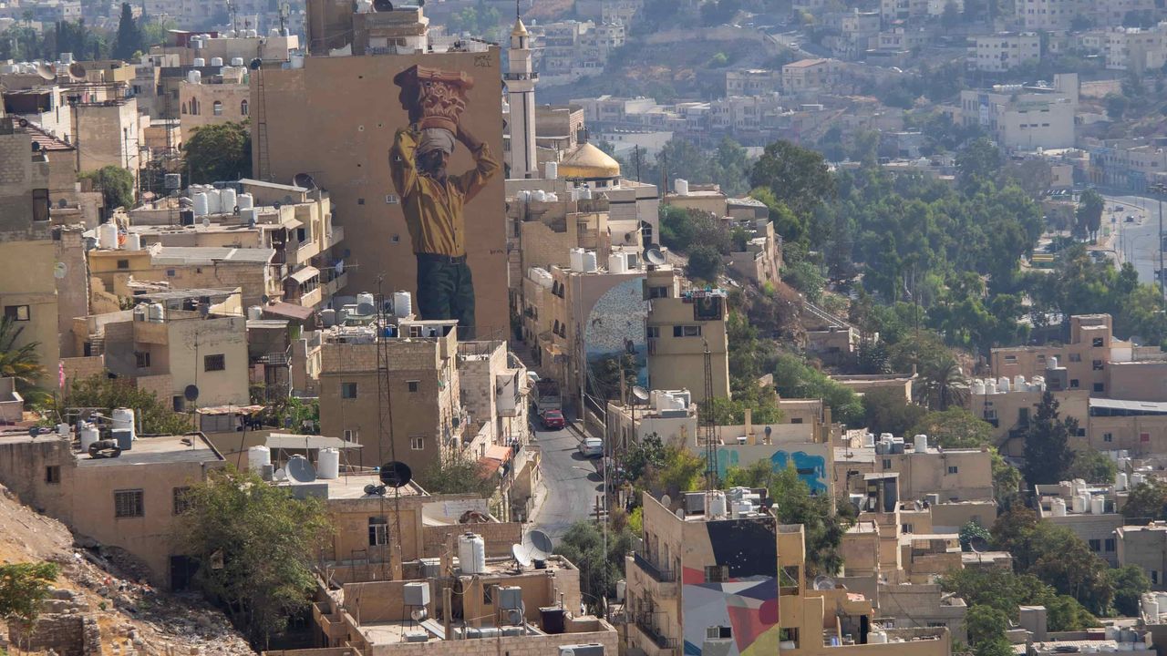 Overview of the buildings of Amman with a street art : a man holding a pot on his head