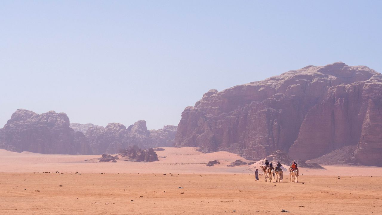 Camels walking in the heat of the rocky orange desert of Wadi Rum in Jordan