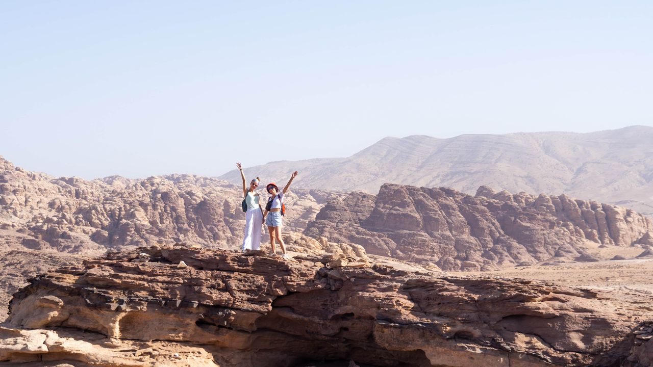 two persons standing in the desert valley on a big rock with their arms up