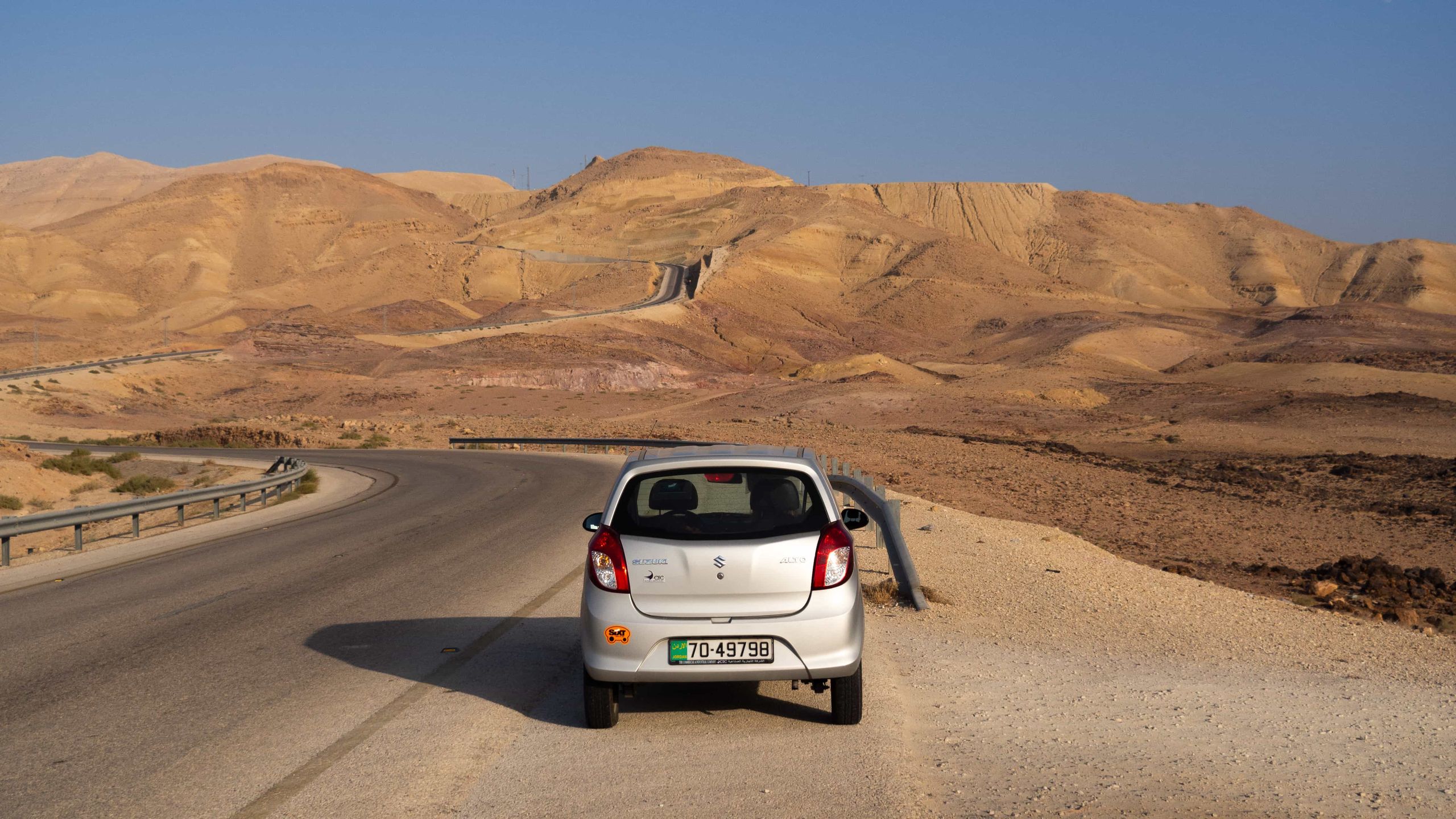 A grey car parked on the side of a road leading into the hilly dry alley