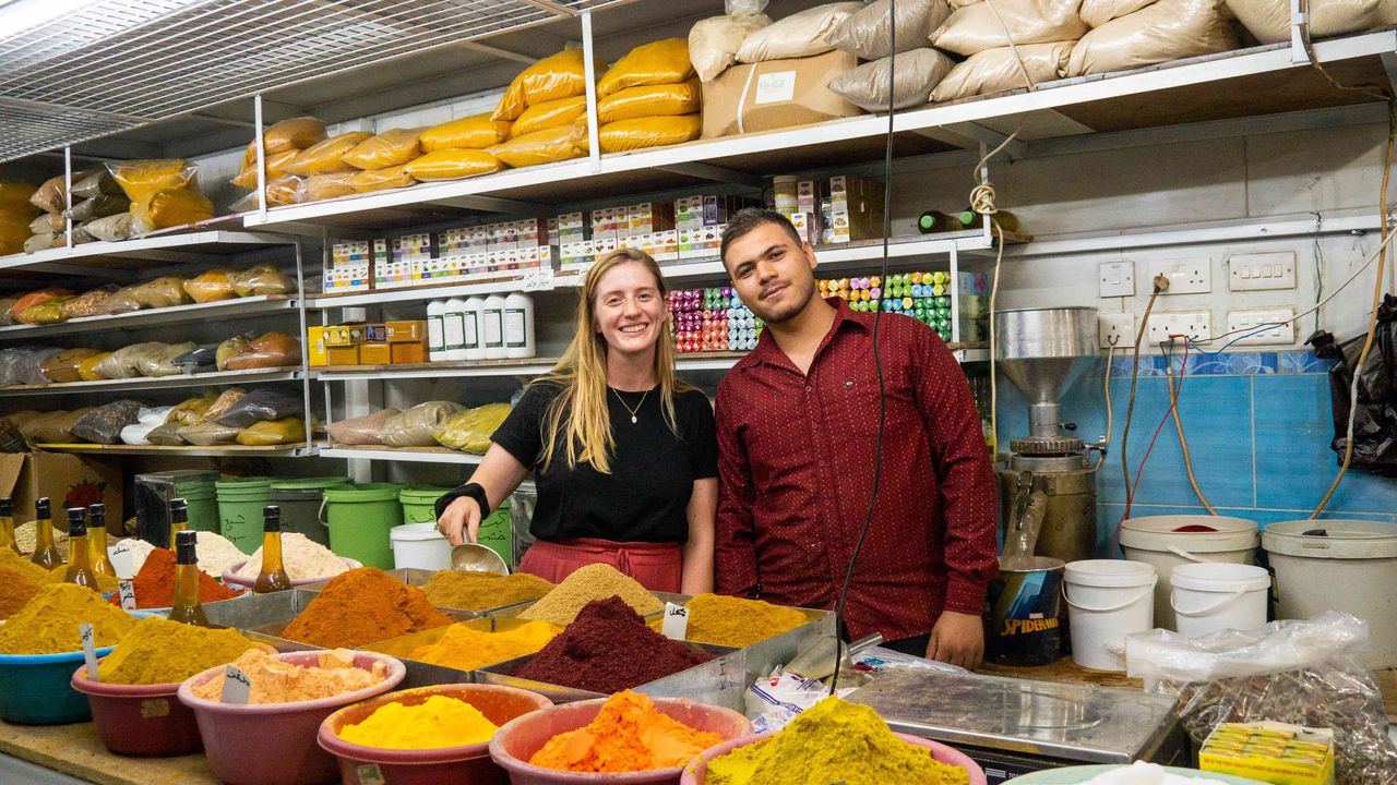 Two persons posing behing spices in a market